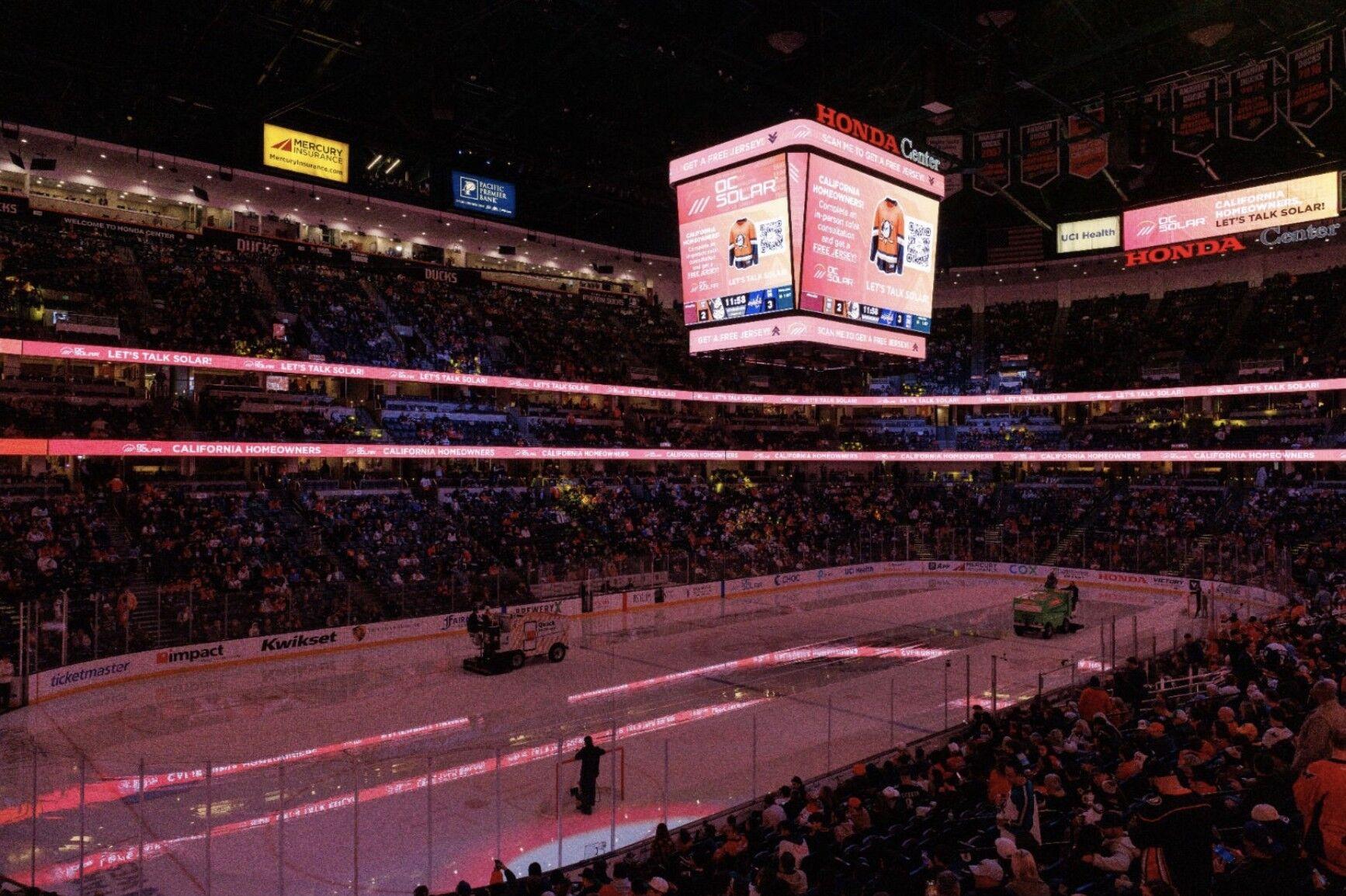 Honda Center bowl-wide with OC Solar's jersey-campaign takeover — the center-hung scoreboard and LED rings lit red with 'Let's Talk Solar' and 'California Homeowners' messaging