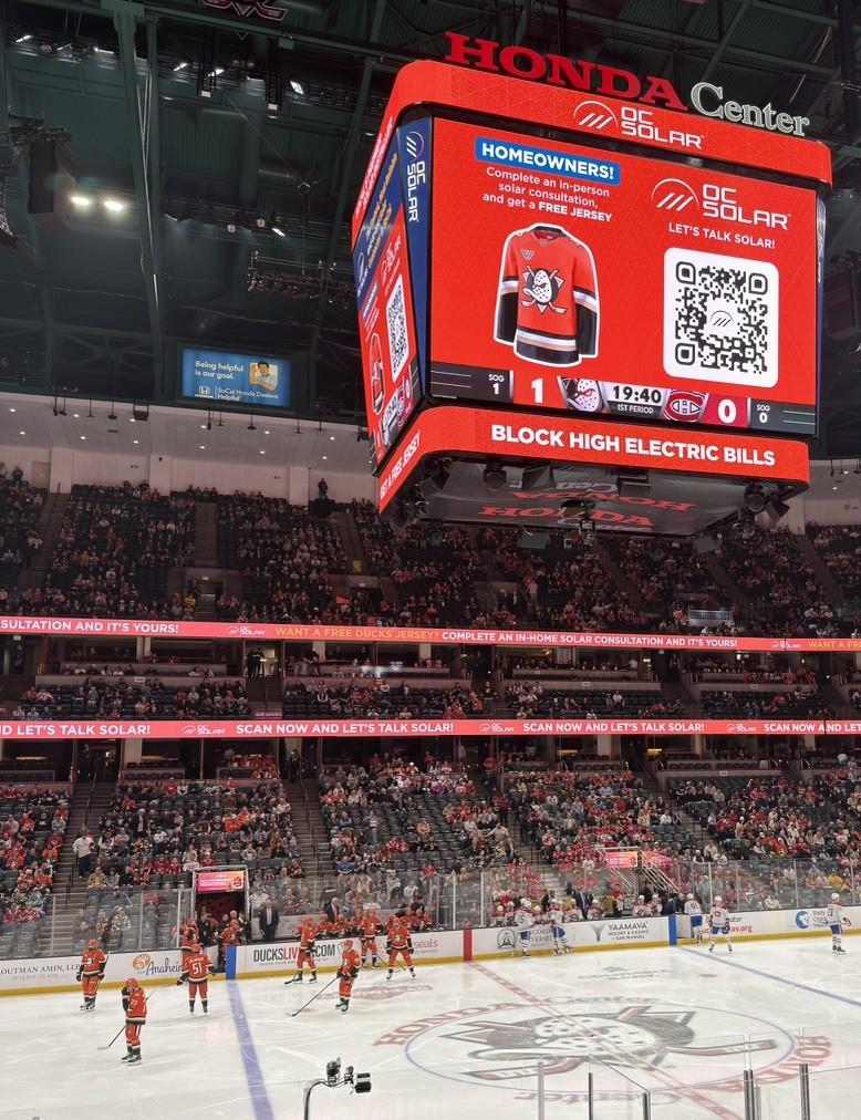 The Honda Center jumbotron during a Ducks–Canadiens game showing OC Solar's free-jersey offer — a Ducks jersey, QR code, and 'Block High Electric Bills' ribbon