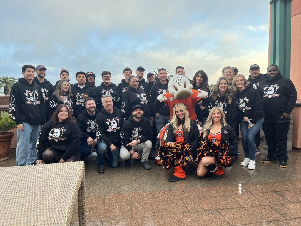 OC Solar team members in matching hoodies posing with the Anaheim Ducks mascot Wild Wing