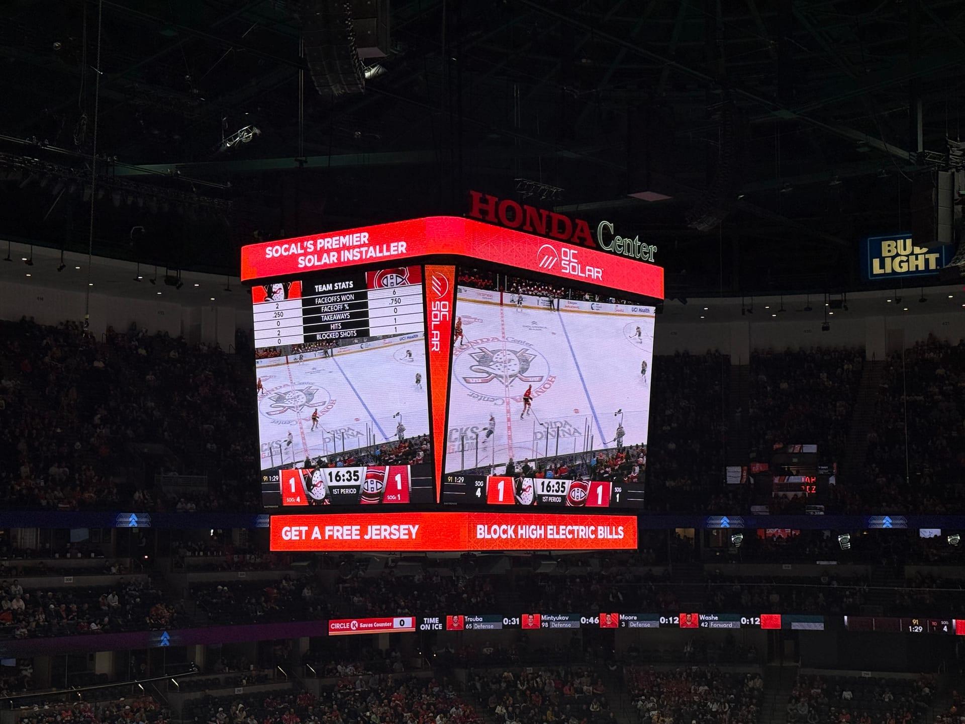 The Honda Center scoreboard during a Ducks game showing OC Solar's offer — 'Get a Free Jersey' and 'Block High Electric Bills'