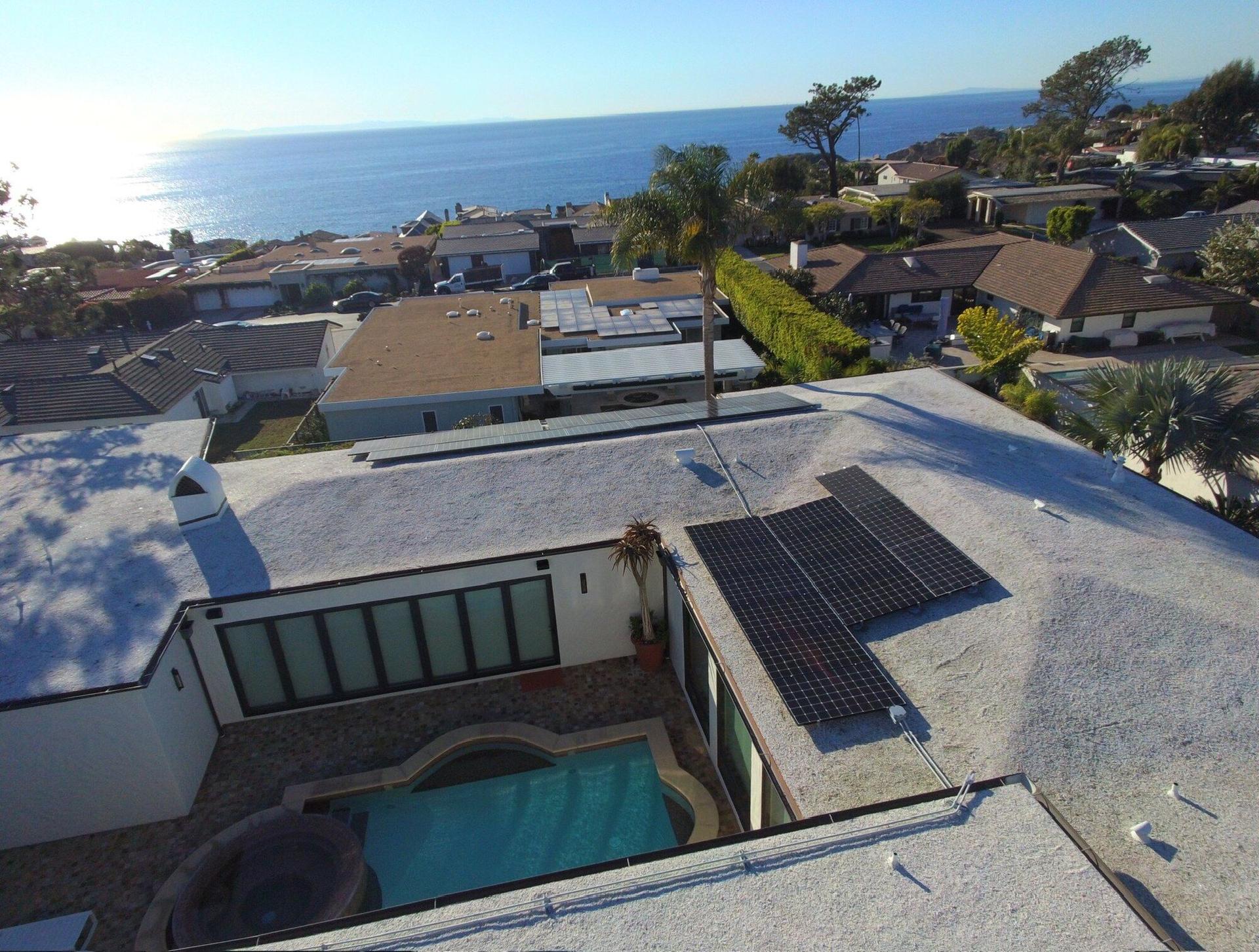 Drone view of an all-black OC Solar panel array on a coastal Southern California home, courtyard pool below and the Pacific Ocean on the horizon
