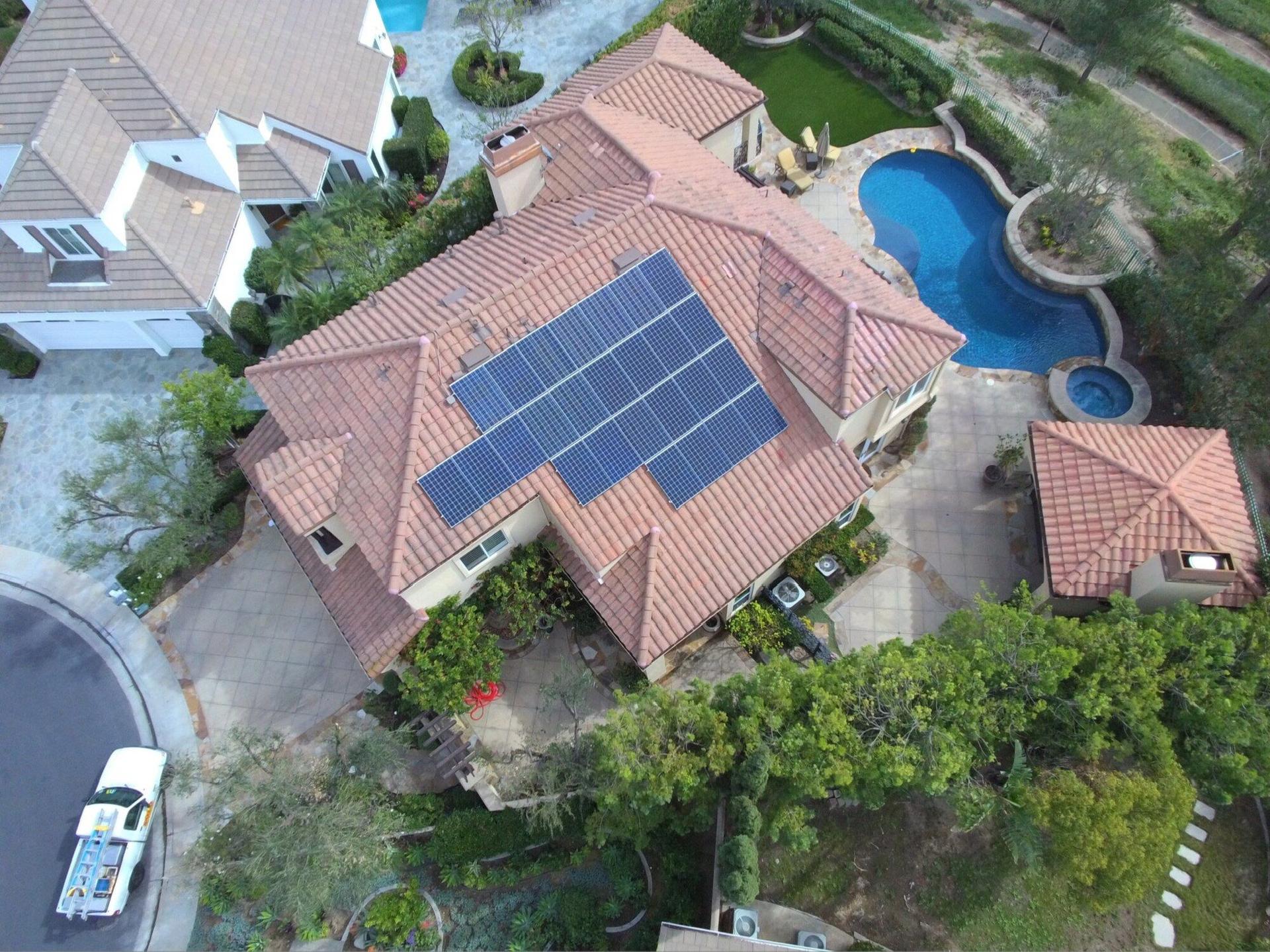 Aerial view of a Southern California estate with an OC Solar panel array on its tile roof and a backyard pool with slide below