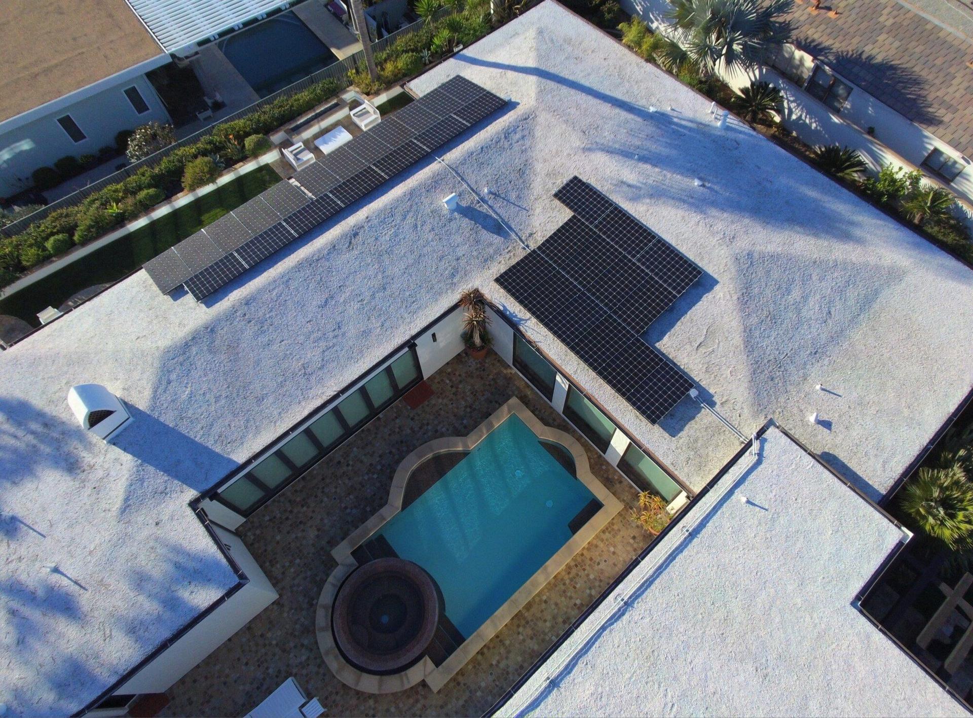 Straight-down drone view of an OC Solar installation with two panel arrays on a white flat roof surrounding a backyard pool and spa