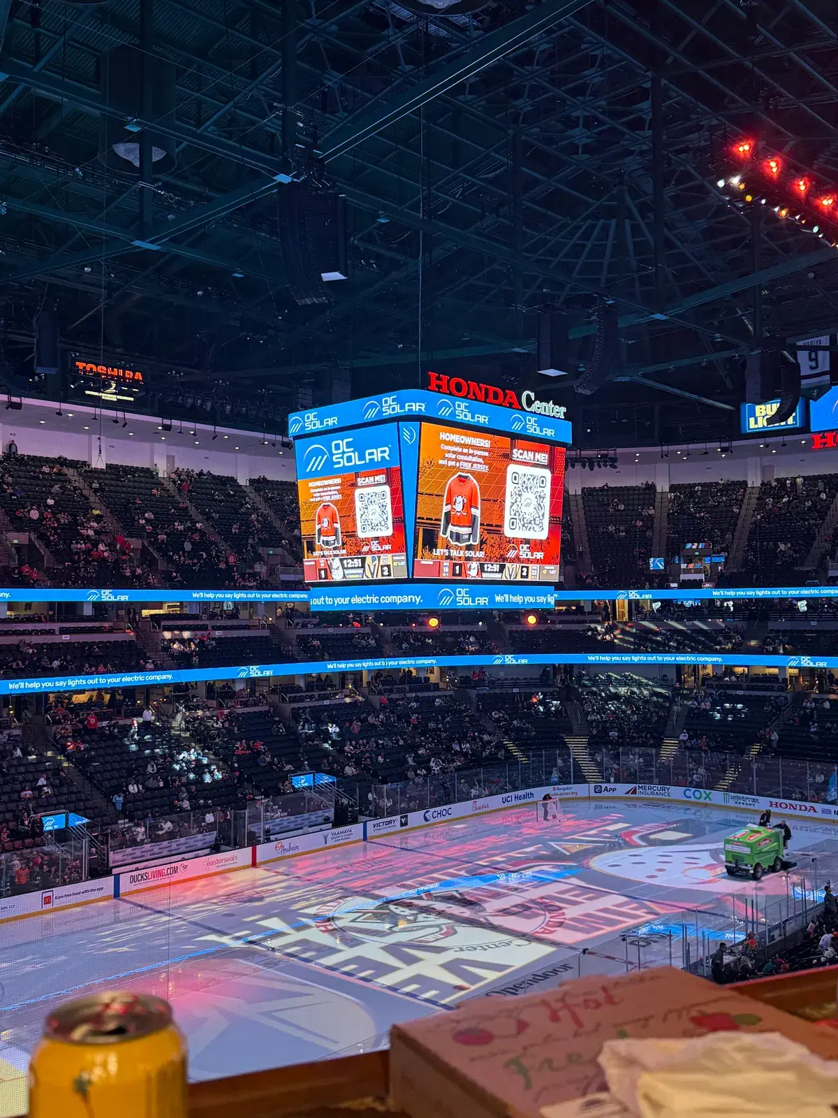 Interior of Honda Center arena with the center-hung jumbotron displaying OC Solar branding above the hockey rink and packed stands.