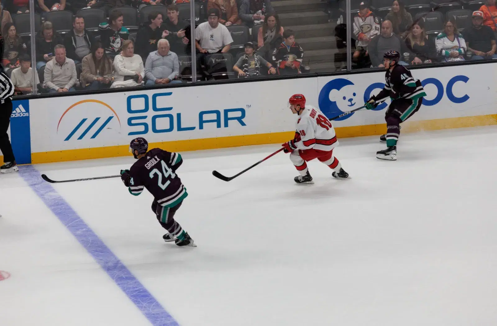 Anaheim Ducks hockey players skating during a game with an OC Solar advertisement displayed on the rink boards.