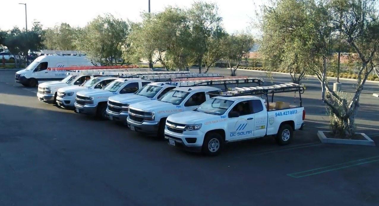 Row of OC Solar install trucks with ladder racks parked in a line at dusk