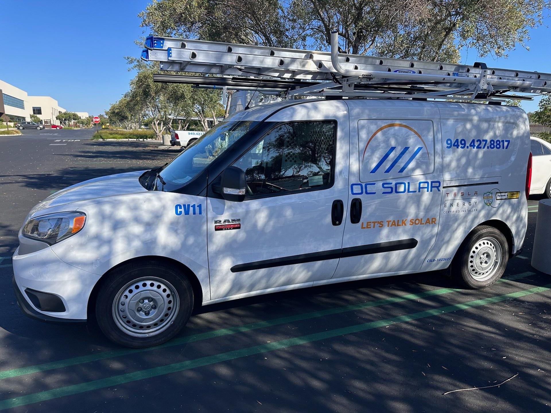 White OC Solar service van with company branding, phone number, and roof-mounted ladders parked outside the Irvine headquarters