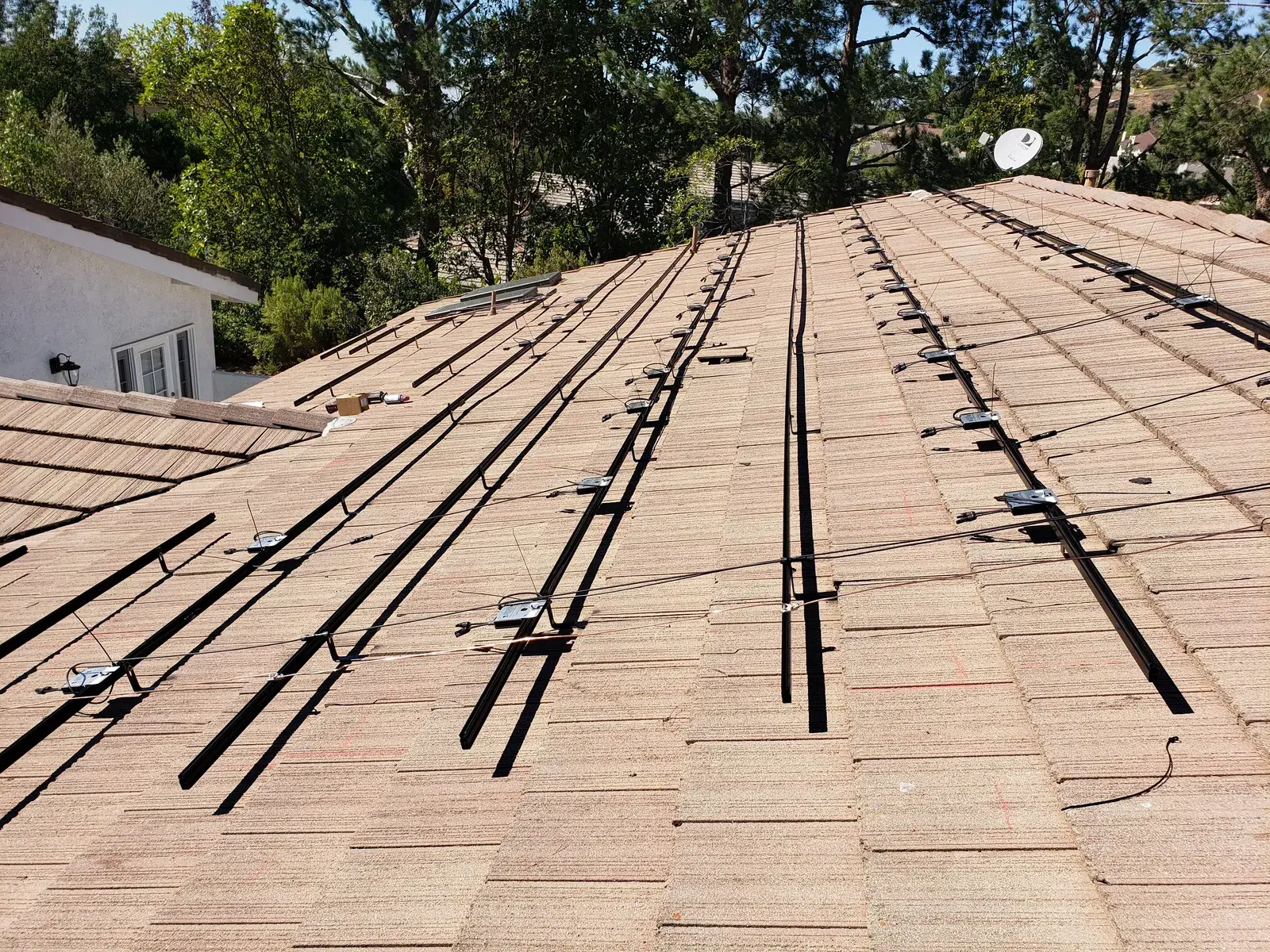 Residential tile roof with solar mounting rails and black electrical wiring laid out, ready for panel installation, under blue sky.