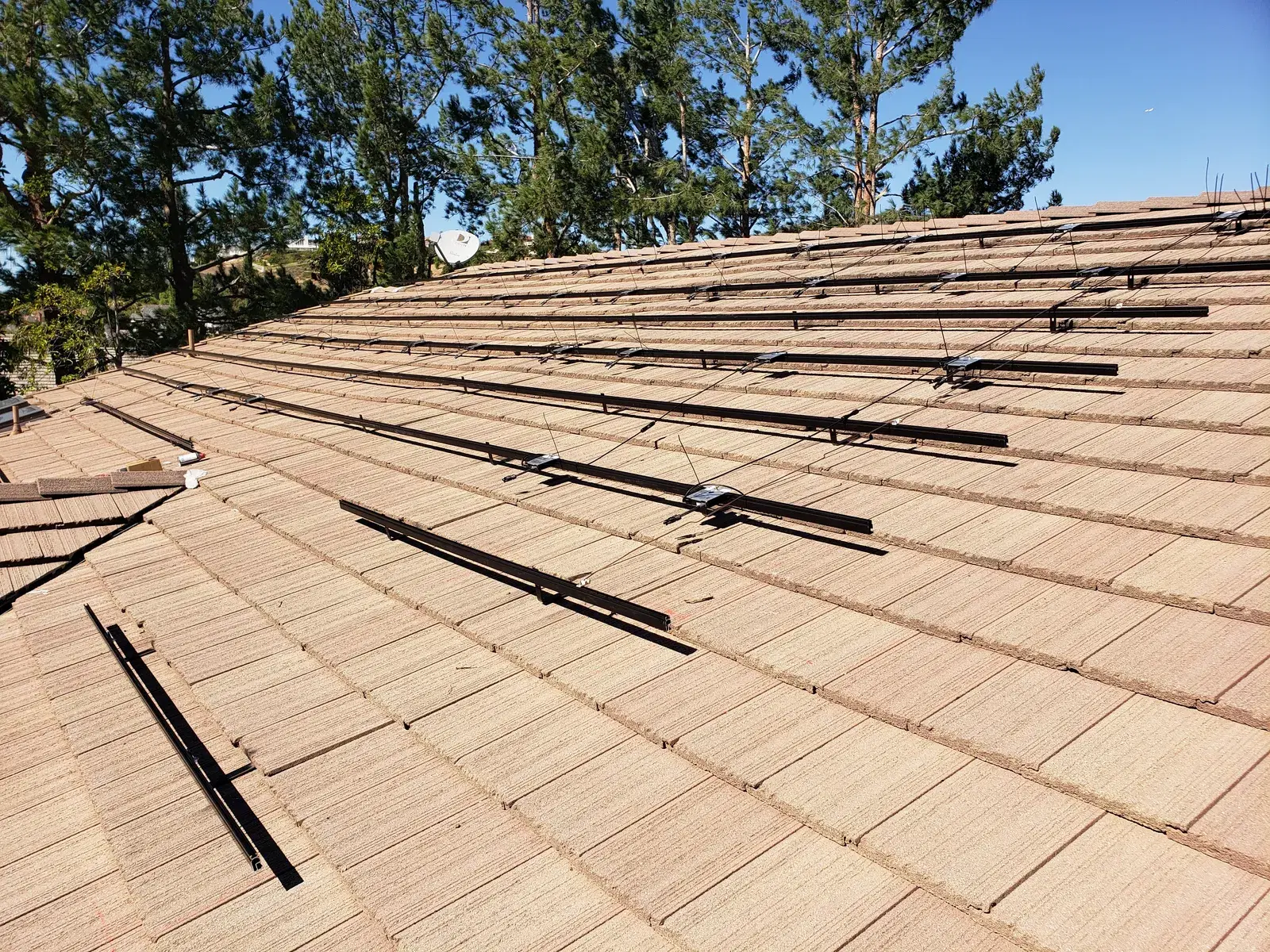 A concrete tile roof under a clear blue sky with black metal solar mounting rails and standoff feet attached but no panels yet installed.