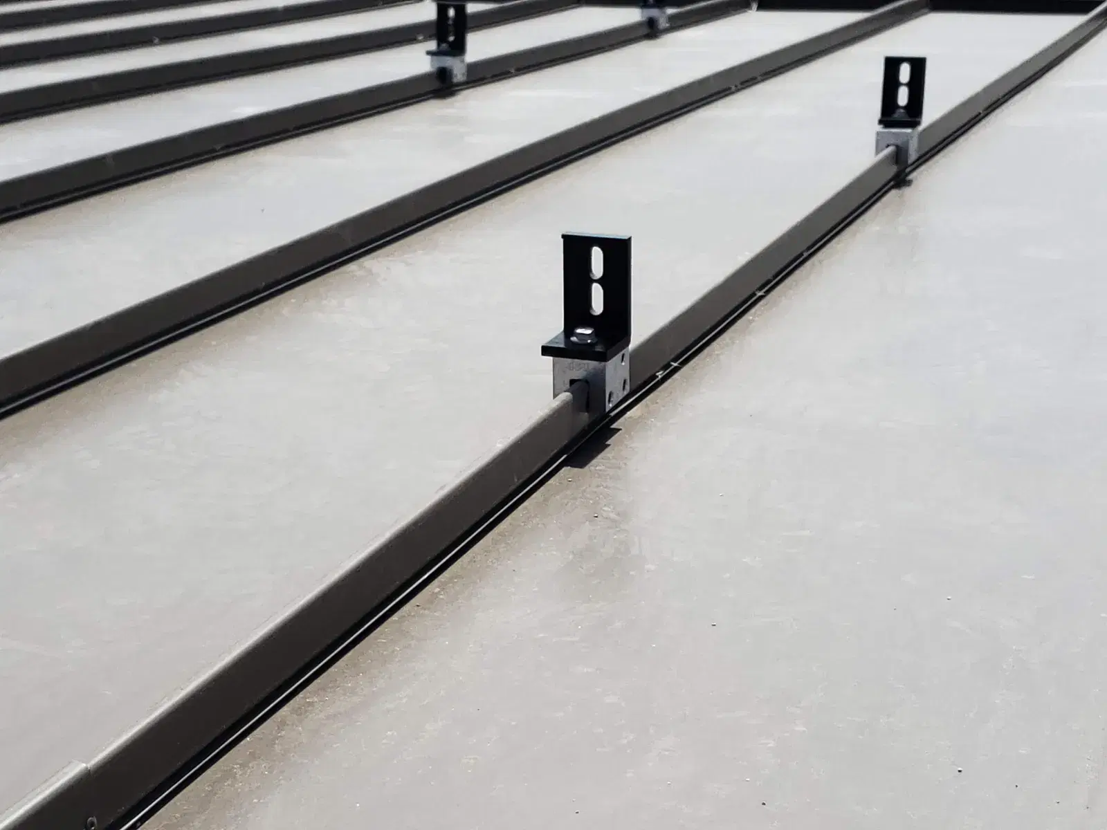 Detail view of black solar mounting brackets clamped to the raised seams of a gray metal roof.