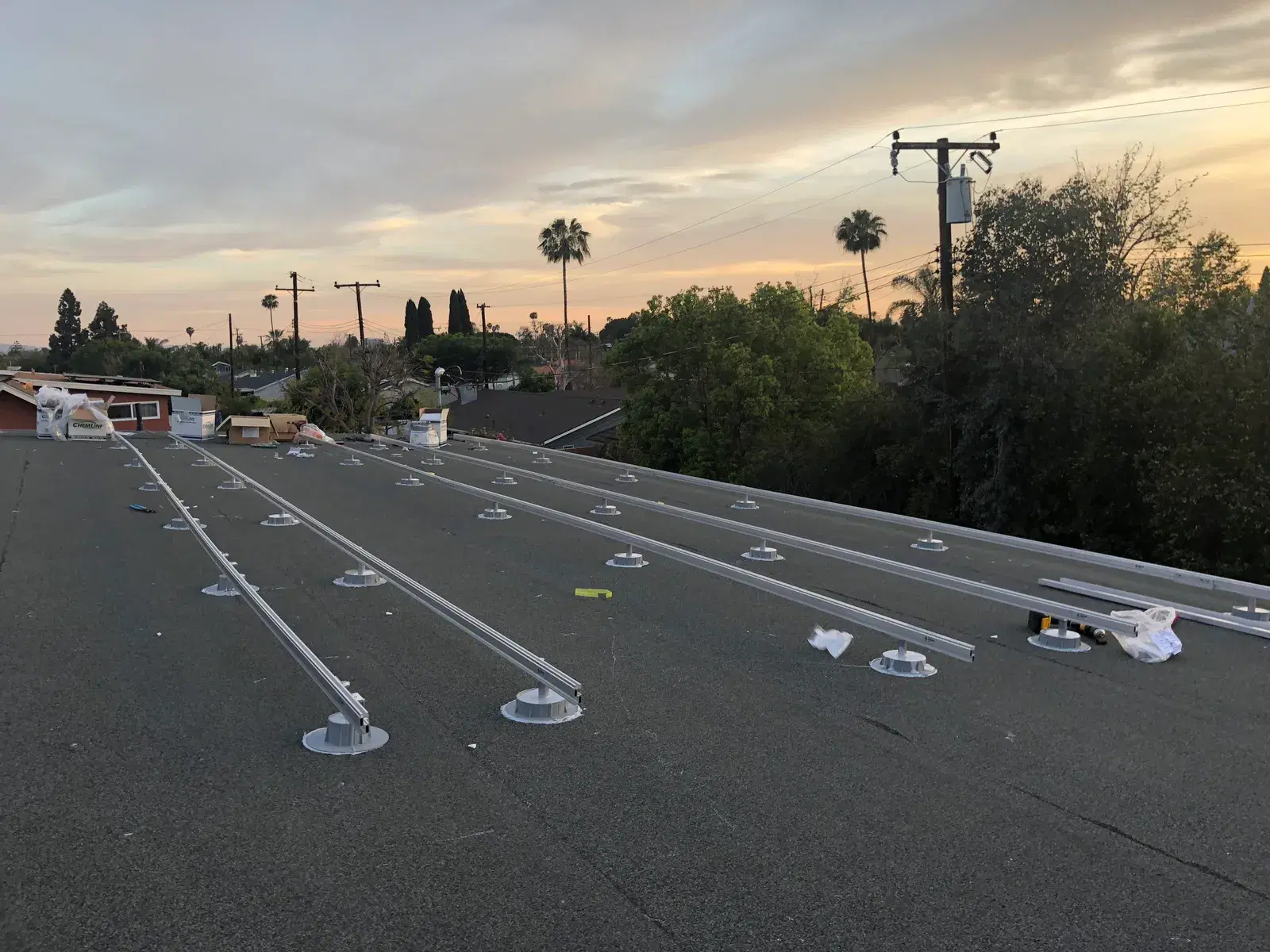 A low-slope residential rooftop at sunset with rows of metal solar mounting rails and flashing feet laid out, no panels installed yet.