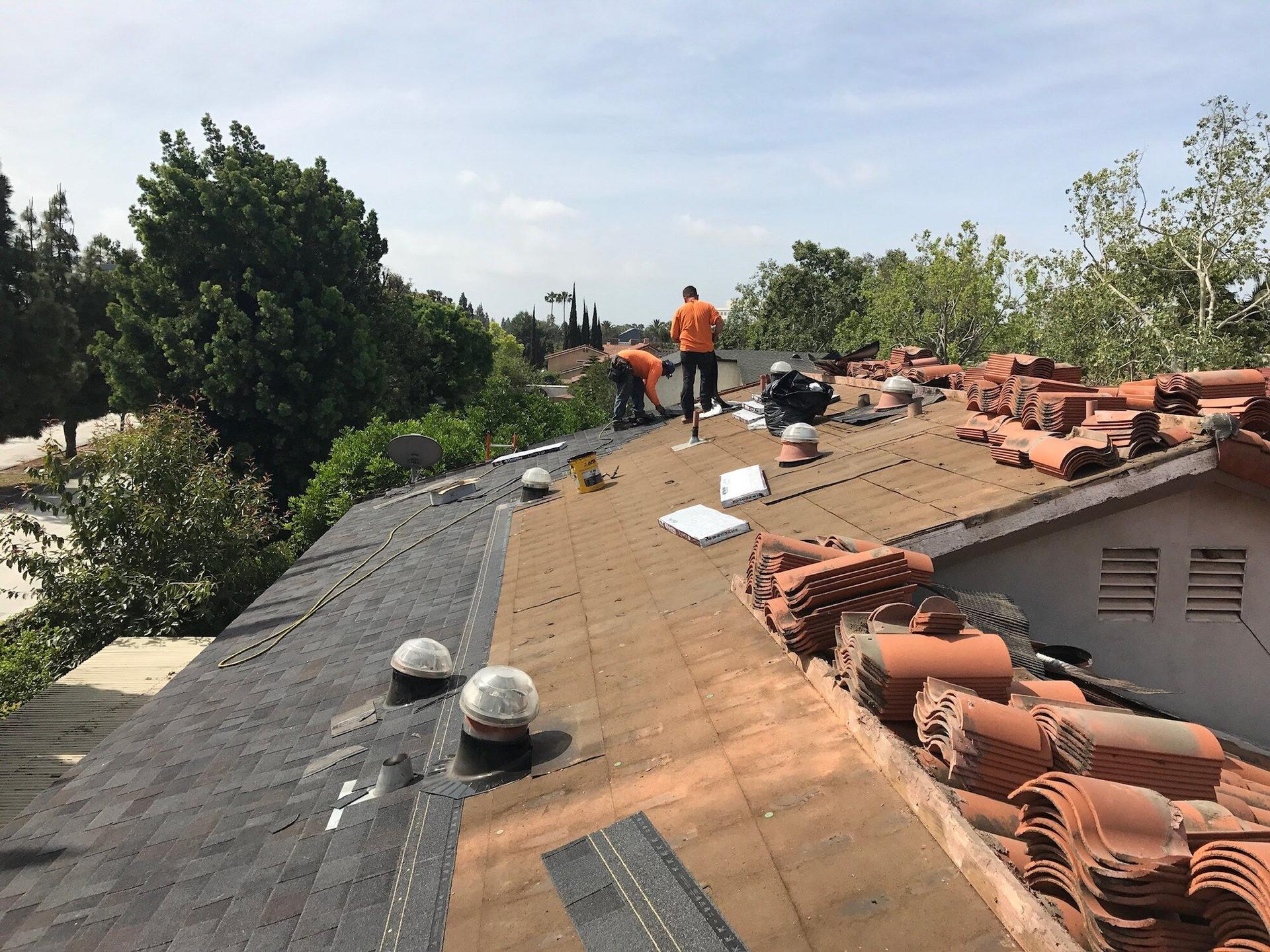 OC Solar installers on a Southern California roof with clay tiles pulled back and stacked, prepping the deck for solar mounting