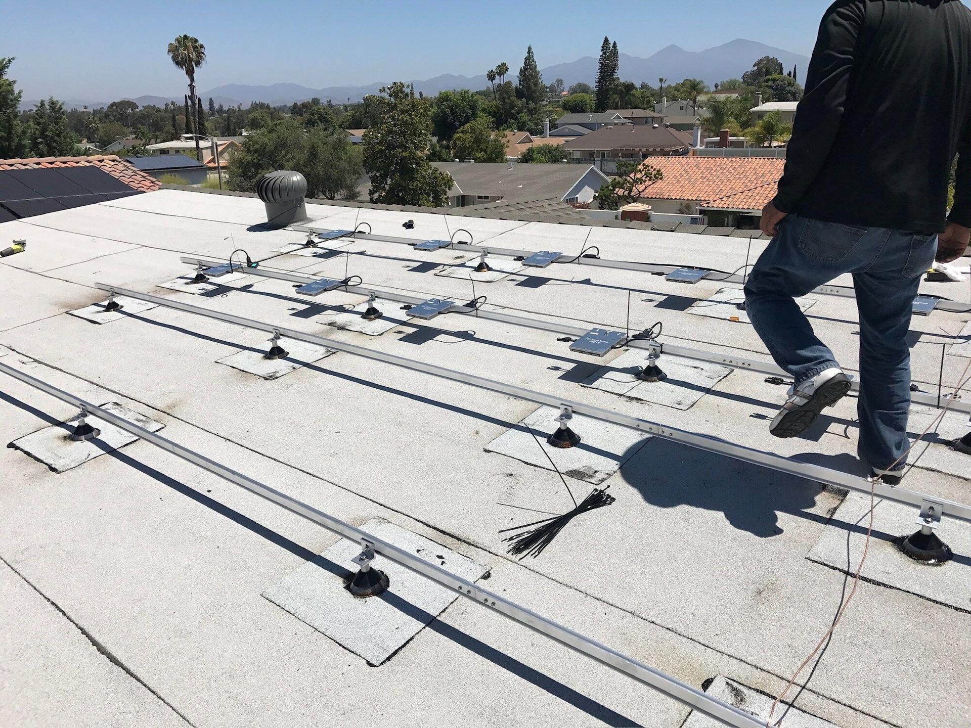 OC Solar installer walking a flat roof where mounting rails and flashed standoffs are laid out before panels arrive