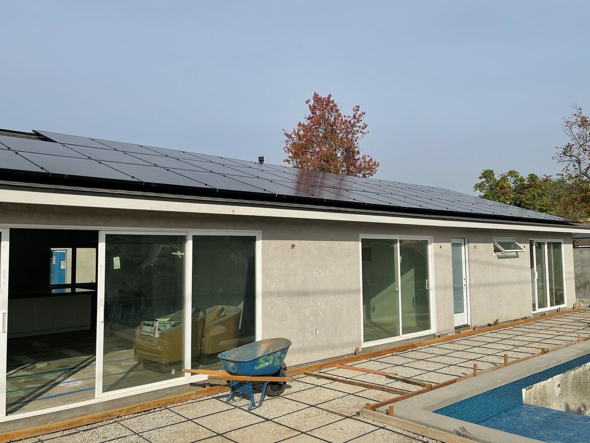 All-black solar panels spanning the full roofline of a modern single-story Southern California home, pool deck in the foreground