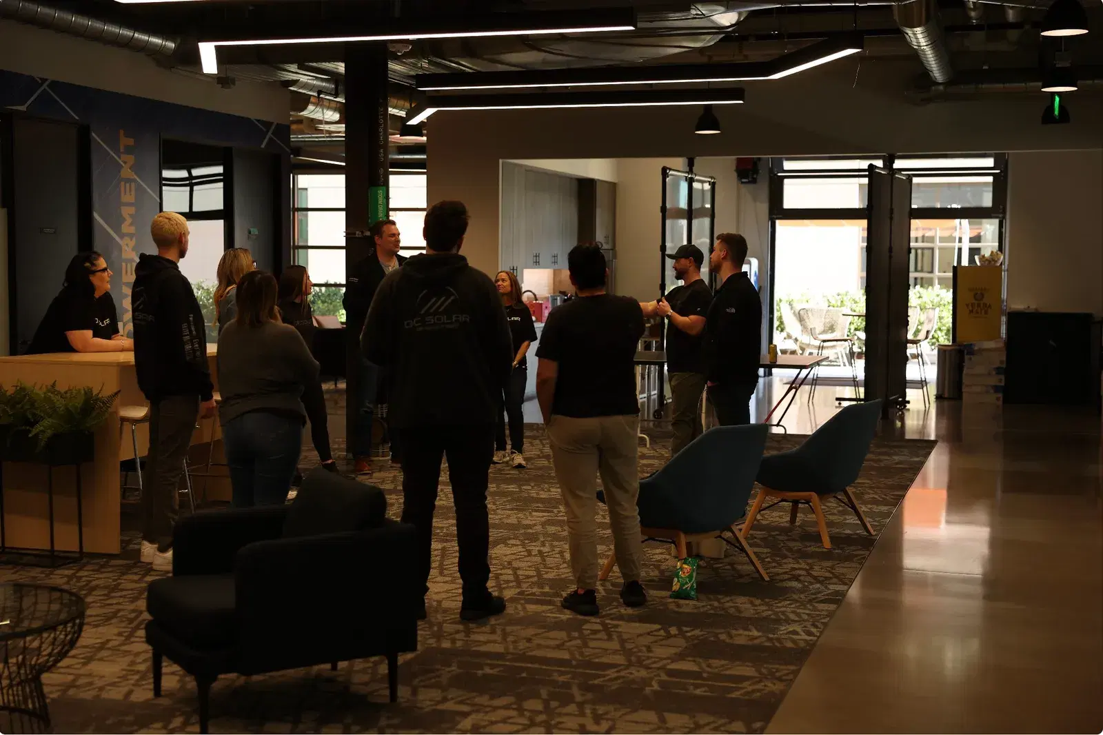 OC Solar employees standing and chatting inside a modern open office lounge with industrial ceilings.