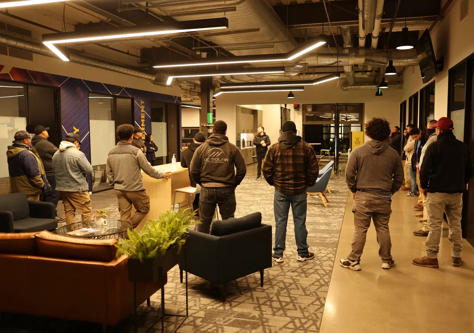 Group of OC Solar employees standing together for a meeting inside the company's modern office lounge.