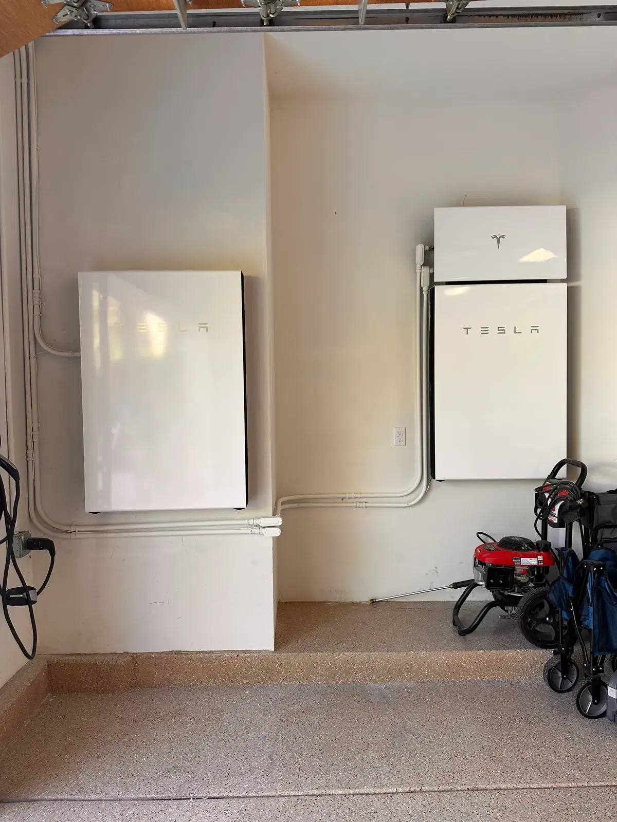 Two white Tesla Powerwall units installed on garage walls with neat conduit running between them.
