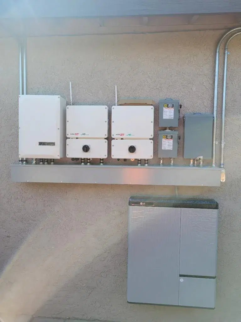Exterior wall-mounted solar inverters, disconnect boxes, and conduit above a gray LG home battery unit.