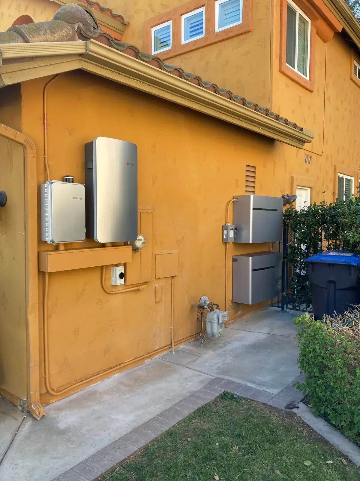 Overhead view of two gray Tesla Powerwall batteries and a Gateway mounted on a tiled rooftop with conduit running to electrical equipment.