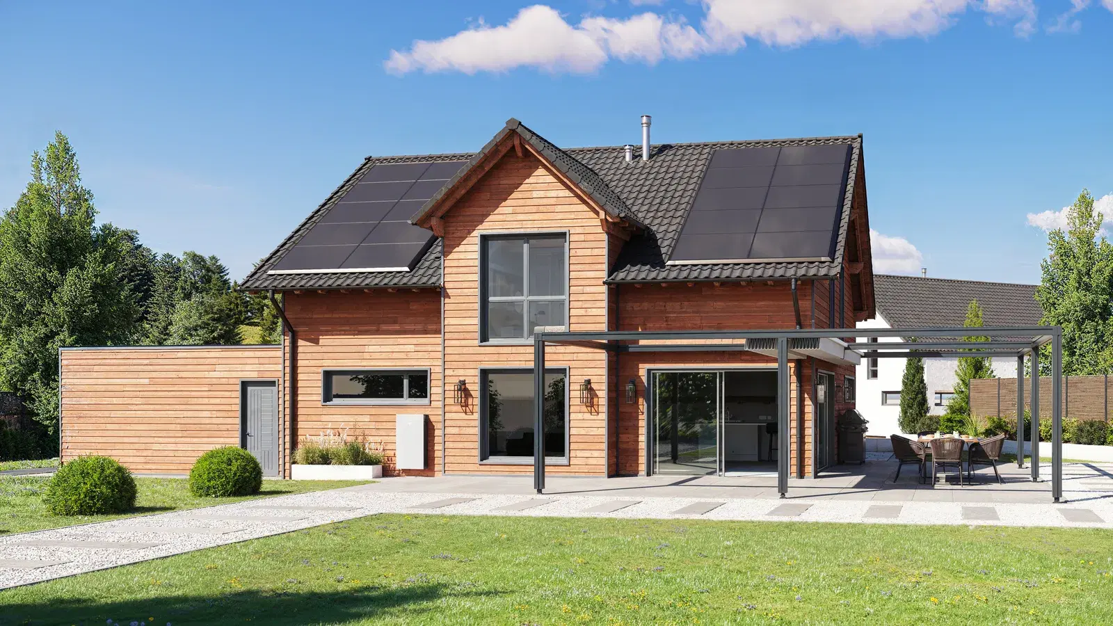 A wooden two-story house with solar panels across both roof faces and a small white battery unit on its side wall, fronted by a green lawn.