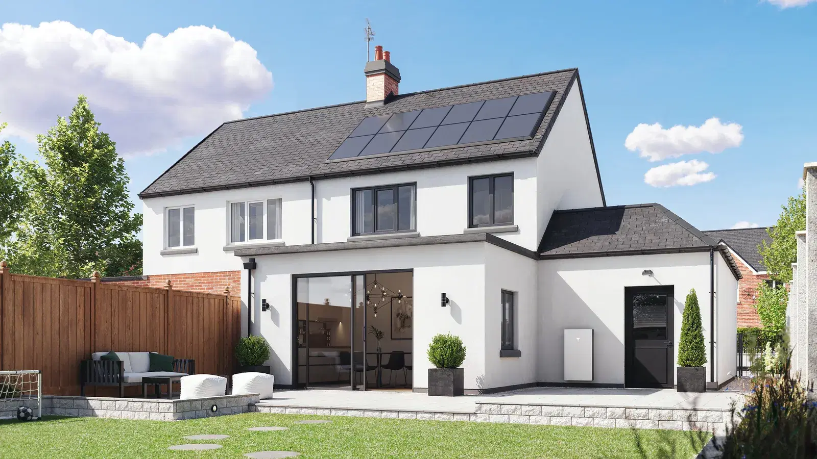 Two-story white house with black rooftop solar panels and a white Tesla Powerwall mounted on the exterior wall beside a landscaped backyard.