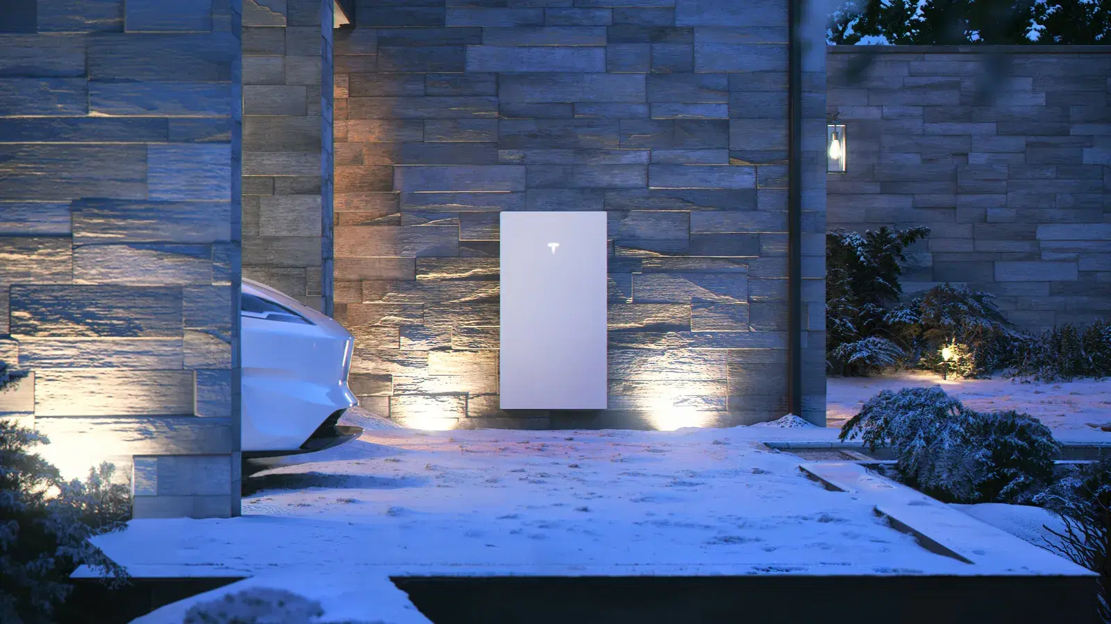 Tesla Powerwall mounted on a stone wall and lit from below at dusk in a snowy yard, with a Tesla car parked alongside.