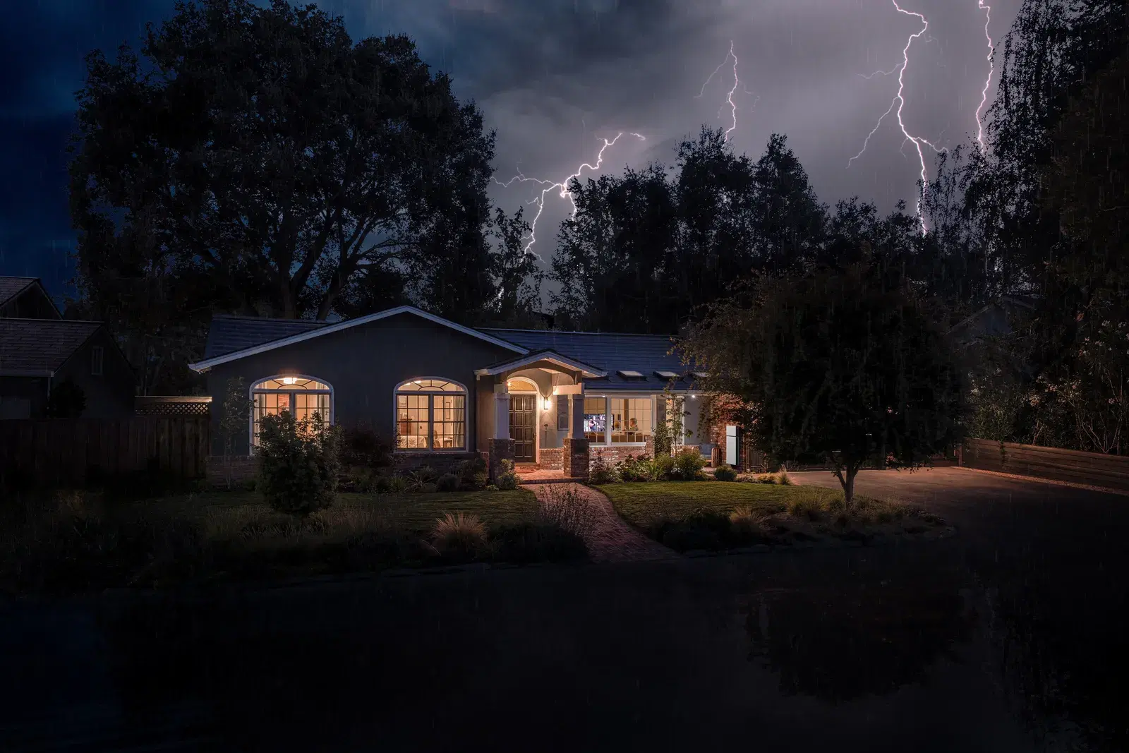 A ranch home stays illuminated during a nighttime lightning storm, with a Powerwall backup unit glowing near the entrance.