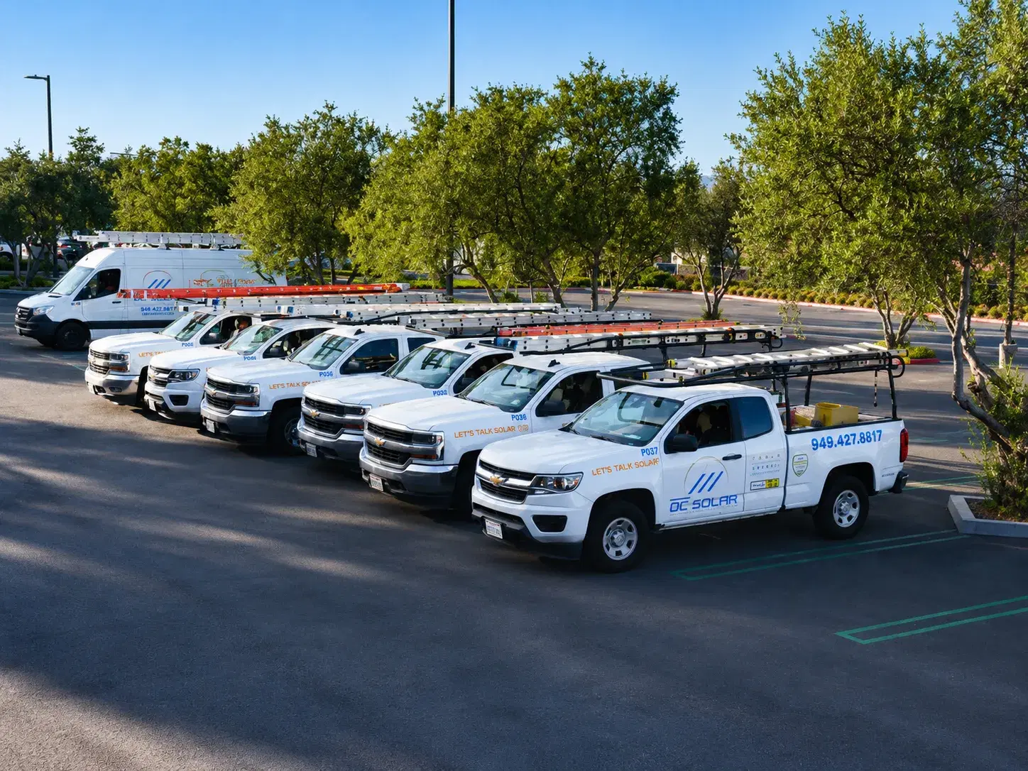 A row of OC Solar service trucks with ladder racks lined up in a sunlit parking lot
