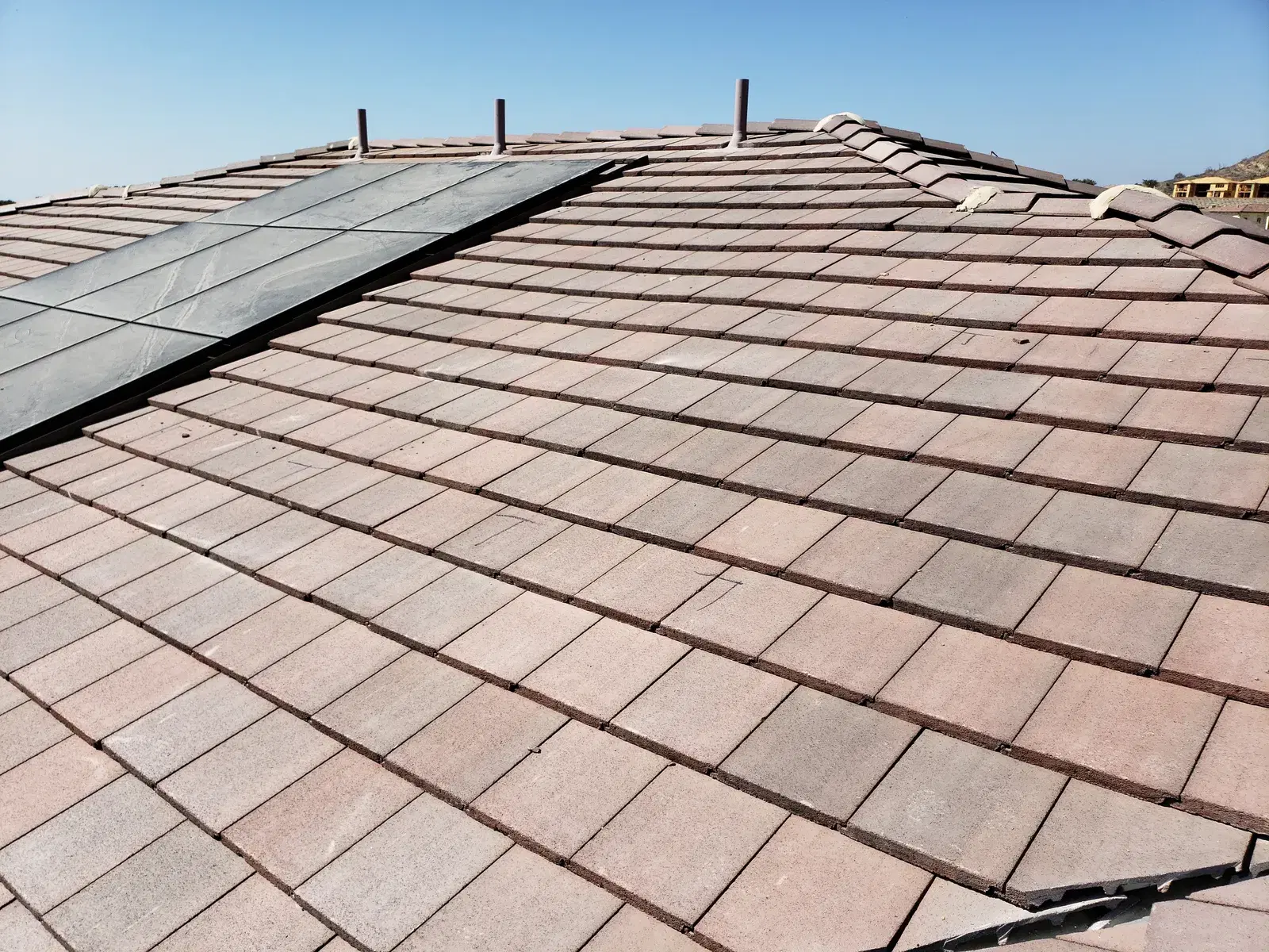 A pinkish concrete-tile rooftop with a row of rectangular dark photovoltaic panels mounted near the ridge against a clear sky.