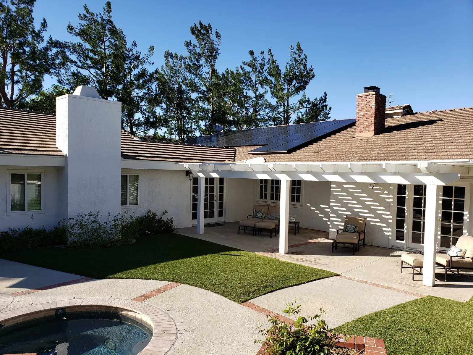 Completed black solar array on a tan tile roof of a white single-story home with a covered patio, lawn, and spa in the foreground.