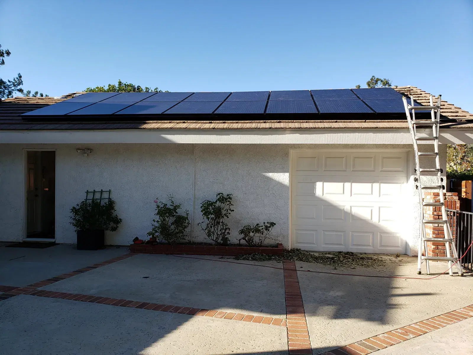 Rooftop solar panel array installed along the edge of a single-story suburban home's roof, with an extension ladder leaning against the roofline.