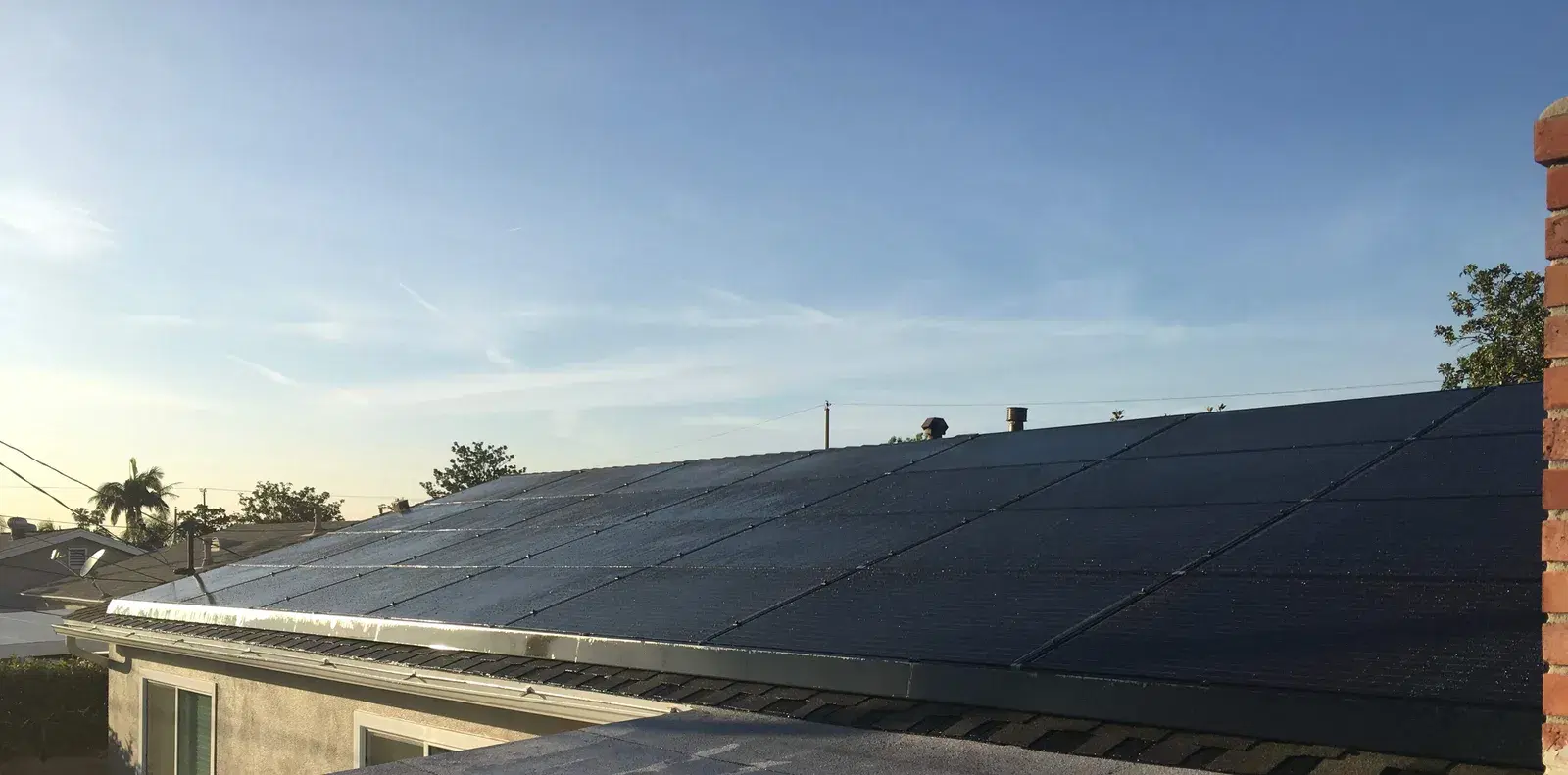 Rows of dark monocrystalline solar panels installed across a residential tile roof against a blue sky.