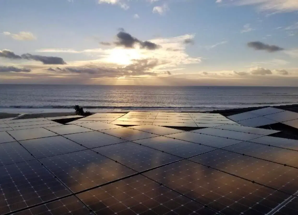 Aerial view of a large rooftop solar panel array overlooking the ocean at sunset.