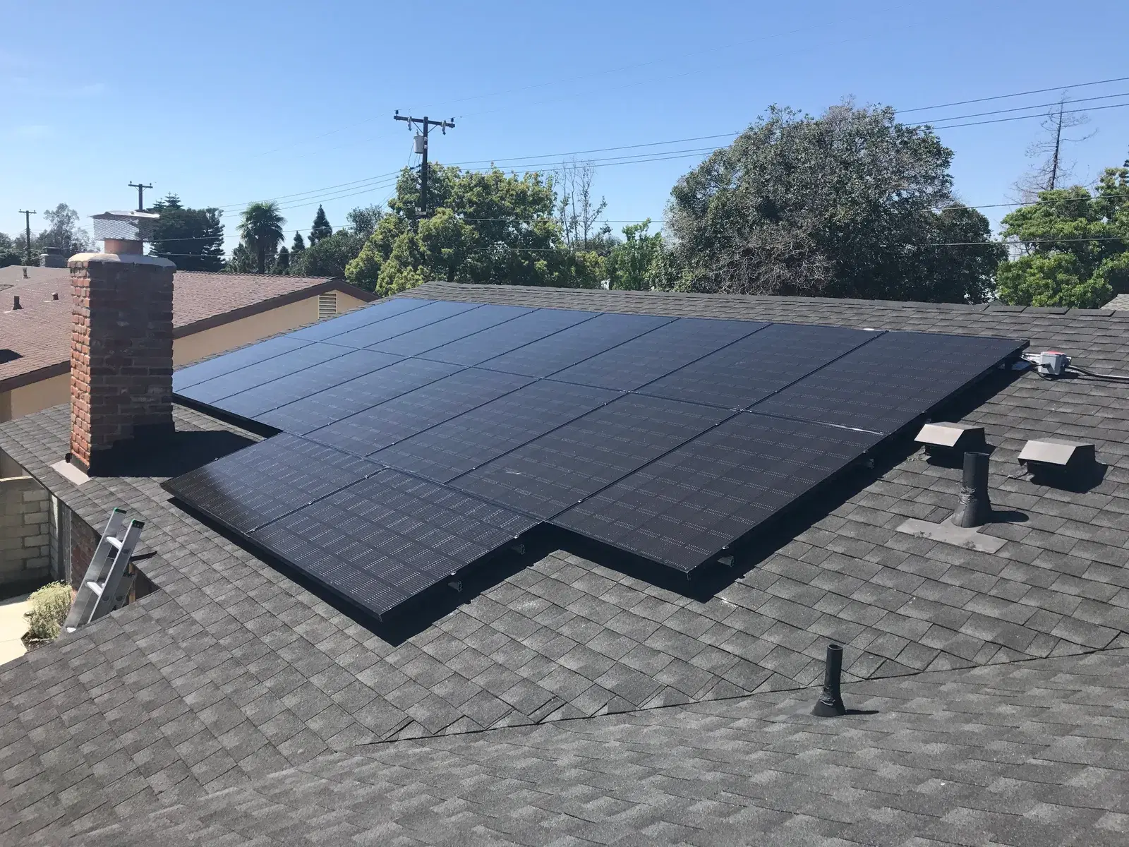 Completed all-black solar panel installation across a gray shingle roof with a brick chimney.