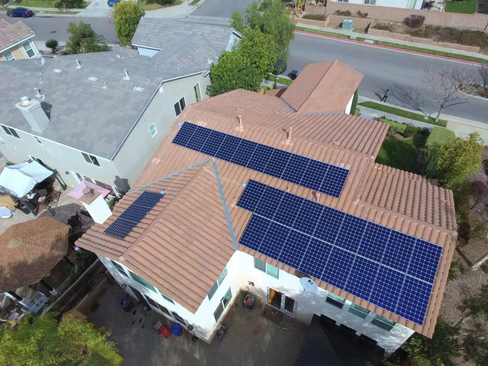 Aerial drone view of solar panels spanning several sections of a red tile roof on a two-story home.