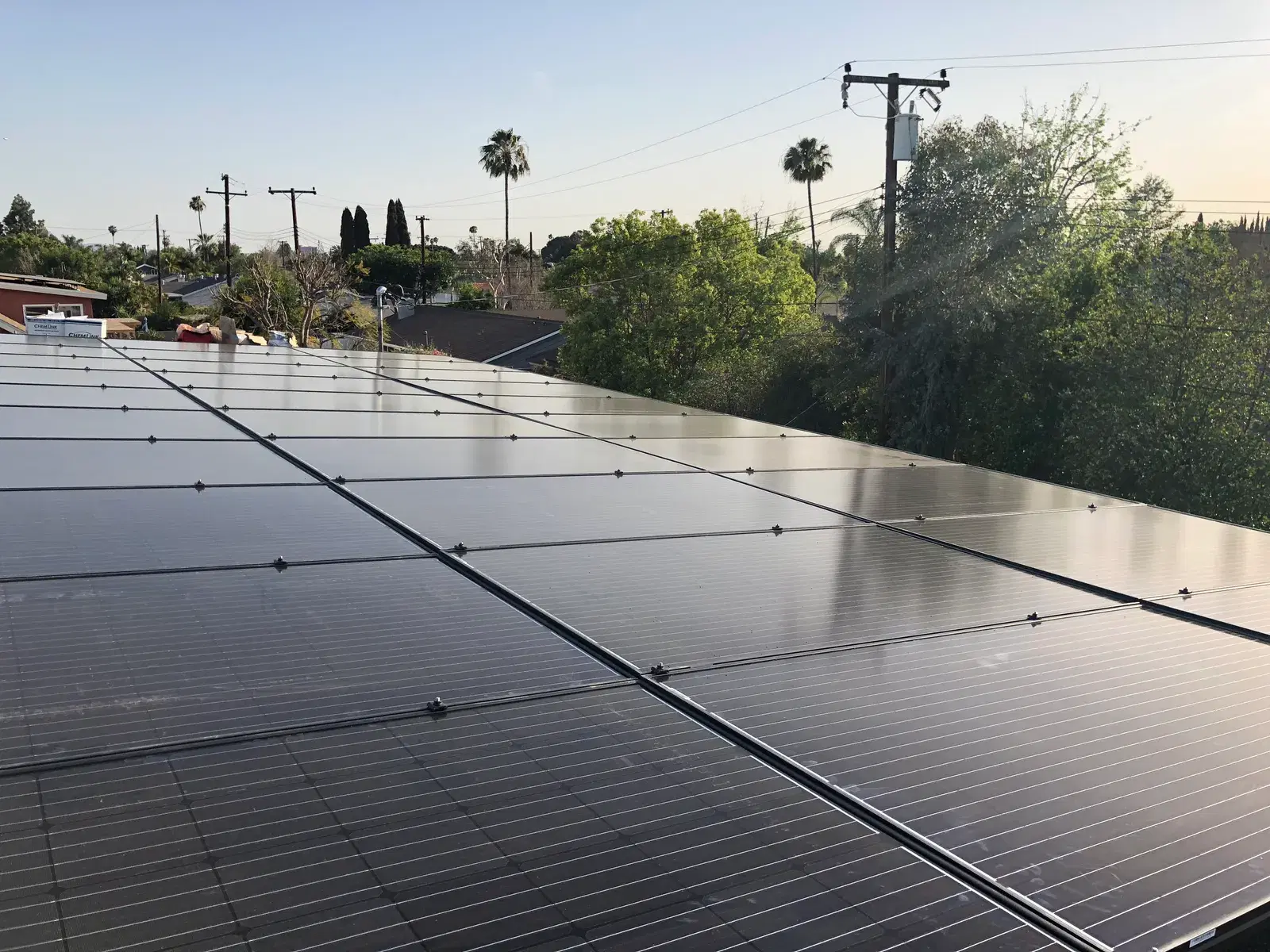 A completed rooftop photovoltaic array catching warm low-angle sunlight, with palm trees and a suburban skyline in the background.