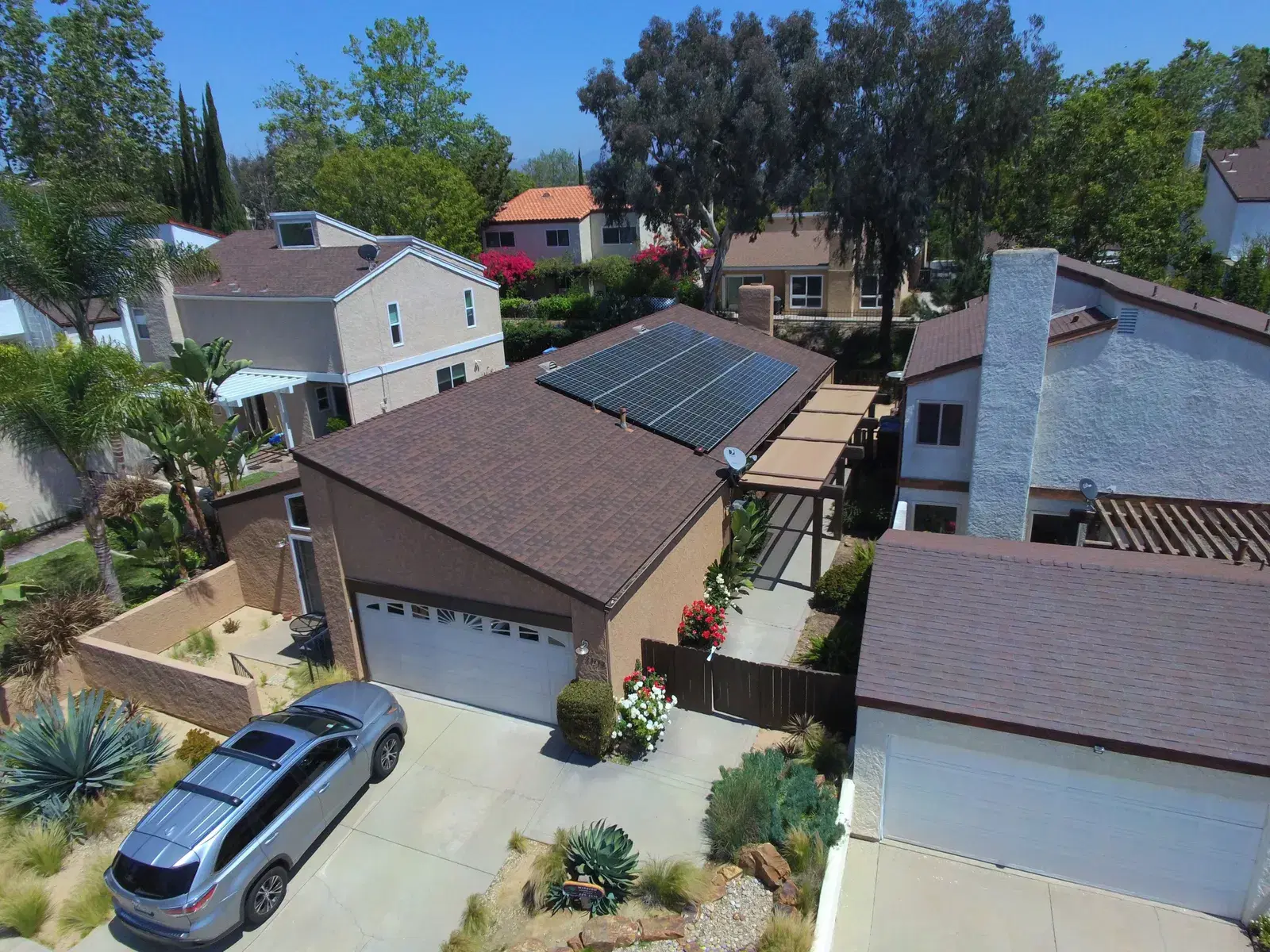 Overhead drone view of a house with a compact solar panel array on the roof and a car parked in the driveway.