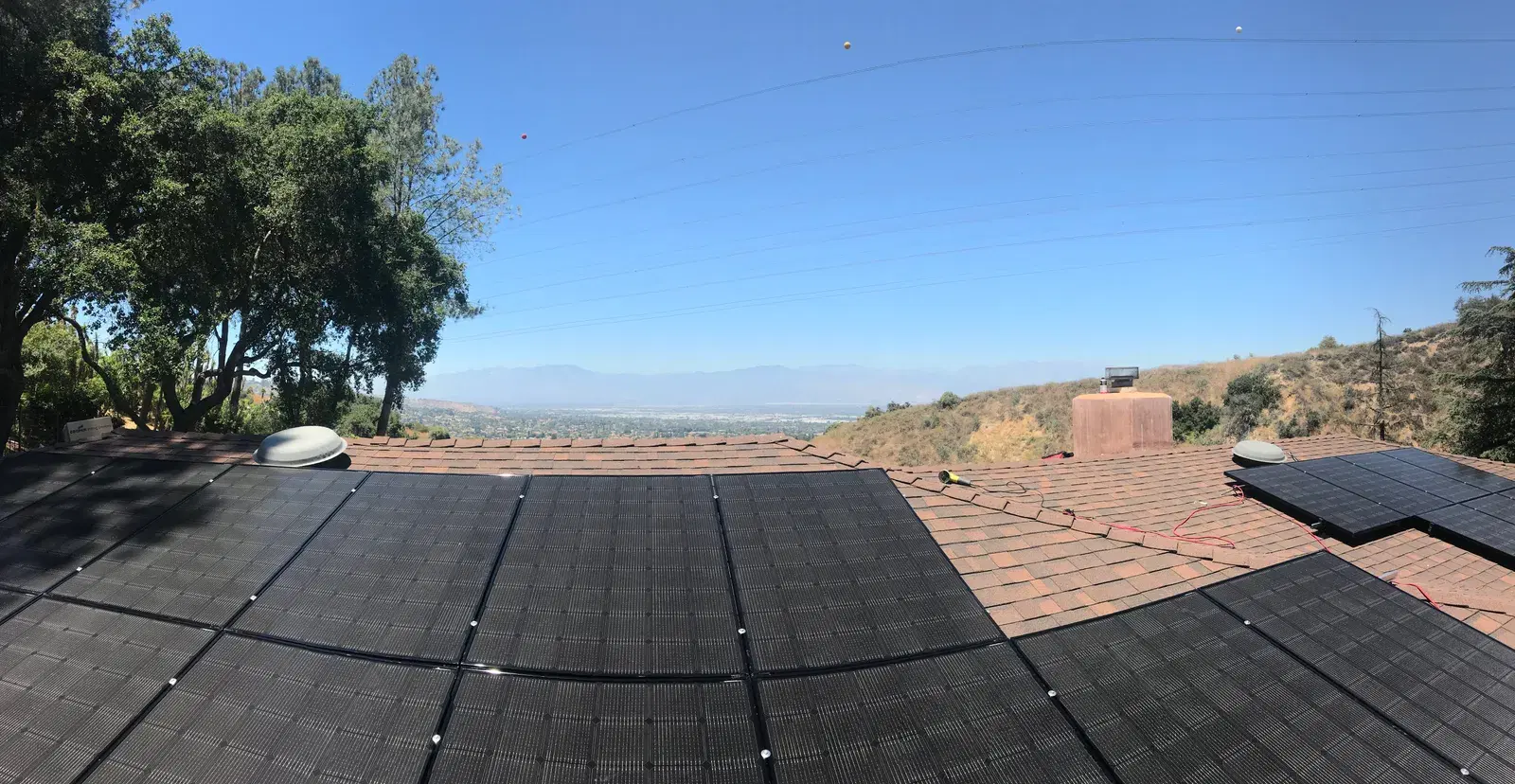 Roof-level view of a full black solar panel array overlooking a hazy valley and distant mountains.
