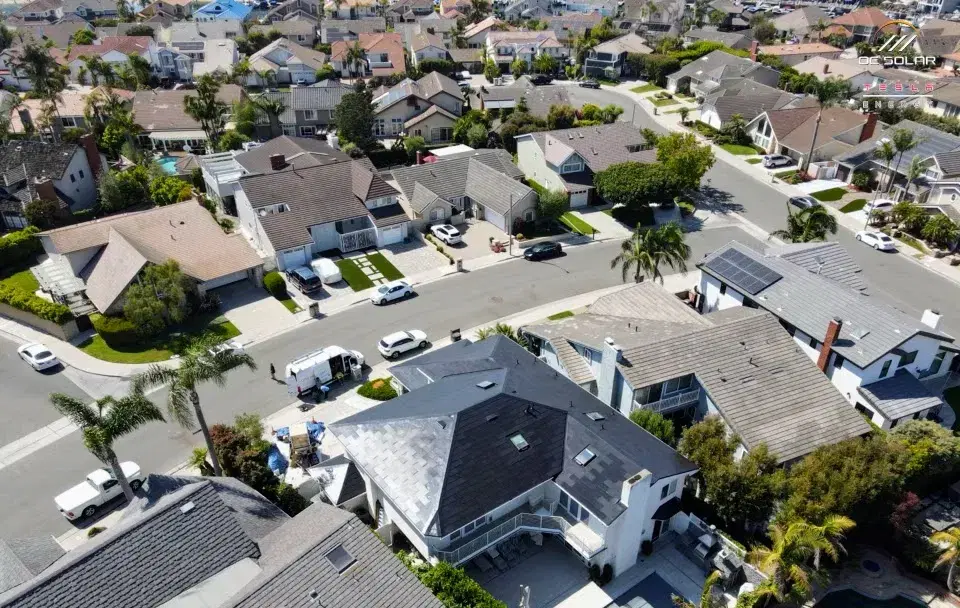 Aerial drone shot of a suburban residential neighborhood with several homes featuring rack-mounted rooftop solar panels and a work van parked on the street.