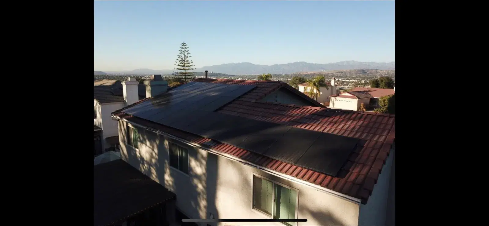 Aerial view of a sleek all-black solar panel array on a hillside two-story home overlooking a valley and distant mountains.