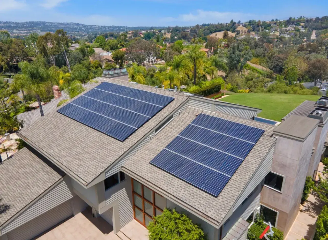 Aerial view of two solar panel arrays on the gray roof of a large modern home above a lush valley.