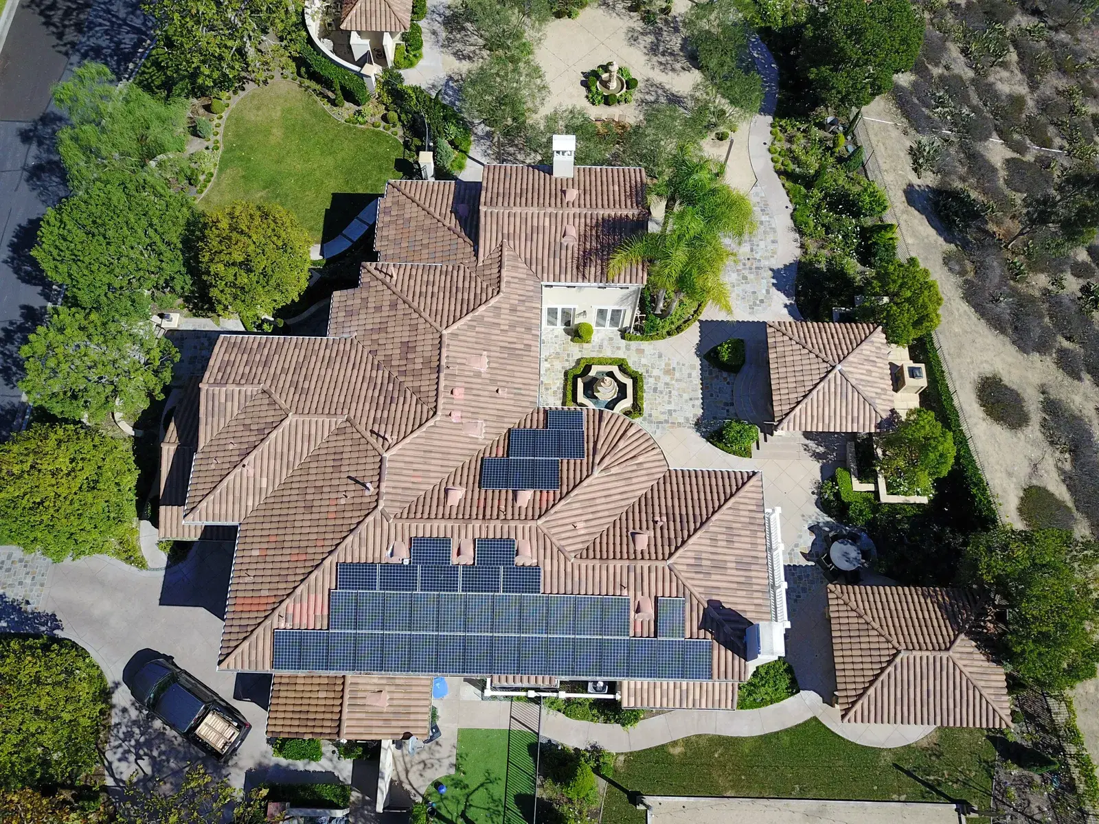 Drone shot looking down on a large terracotta tile-roof home with solar panels and a central landscaped courtyard.