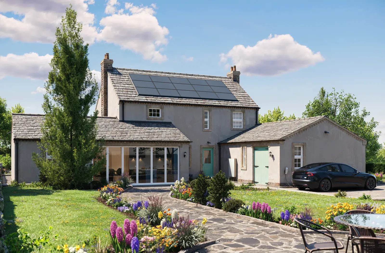 A rural stone home with a black solar panel array on the main roof, a flowering garden in front and a car parked by the garage.
