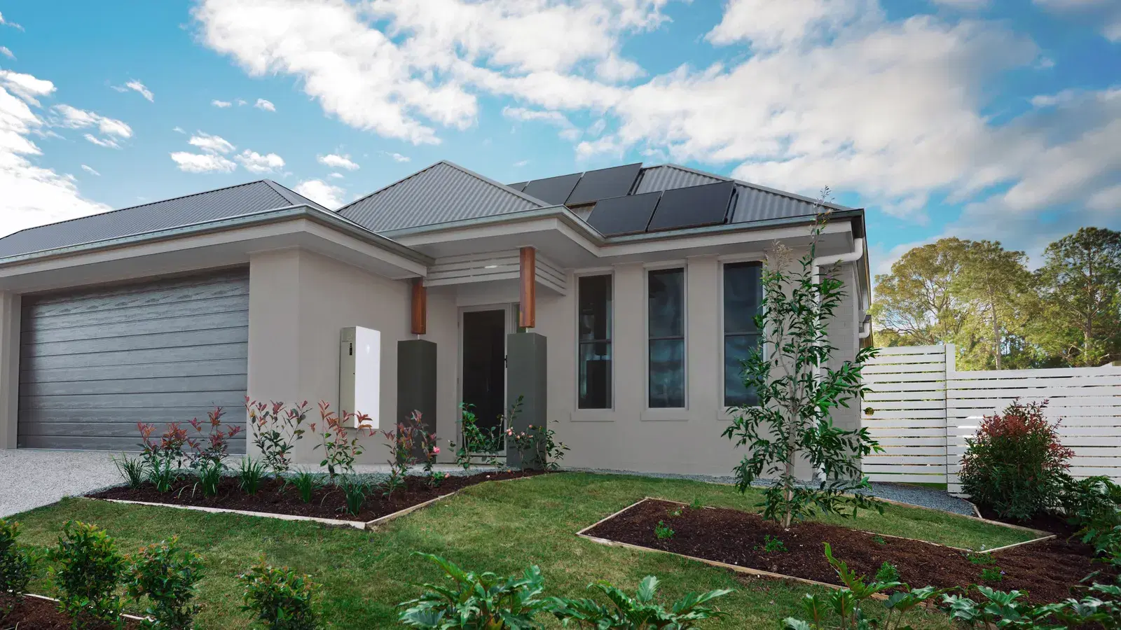 A modern single-story home with a small solar panel array on a gray metal roof and a landscaped front yard.