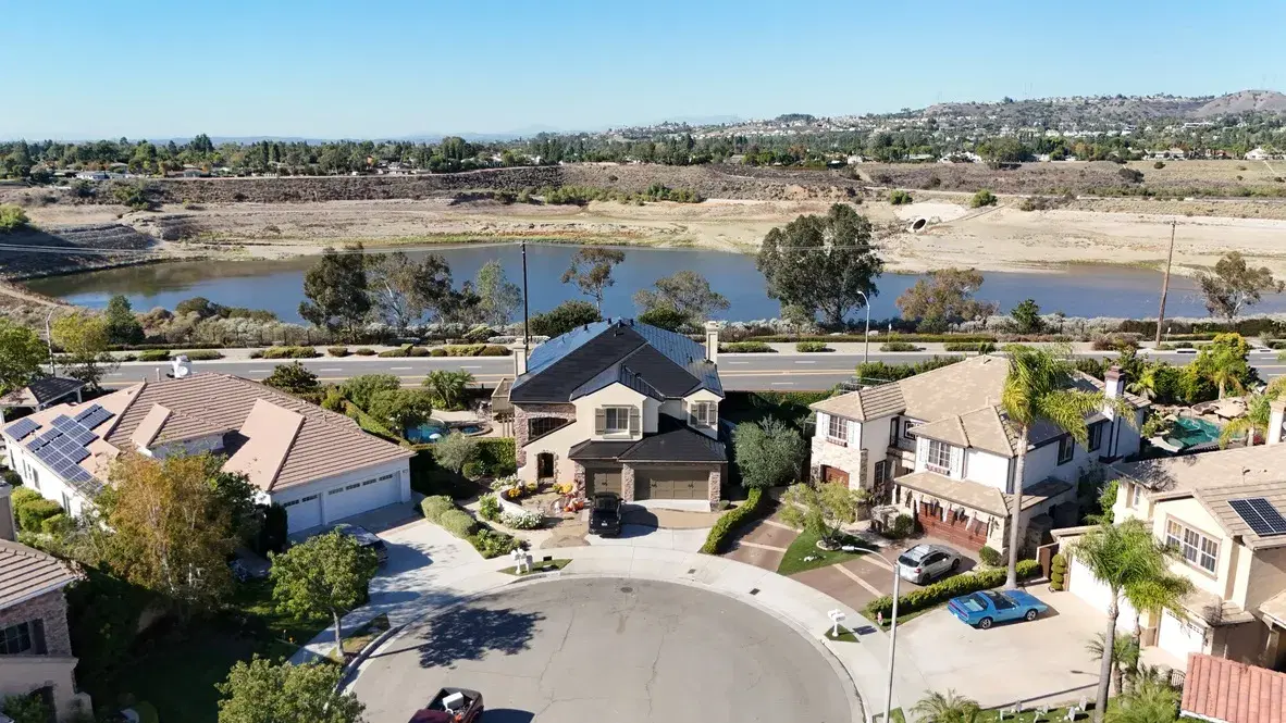 Aerial shot of a suburban cul-de-sac with rooftop solar panels on several homes overlooking a lake.