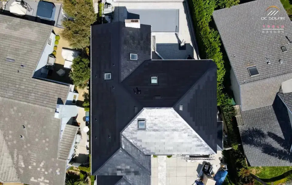 Overhead drone shot of a residential home with a Tesla Solar Roof made of smooth dark glass solar shingles covering the entire roof surface.
