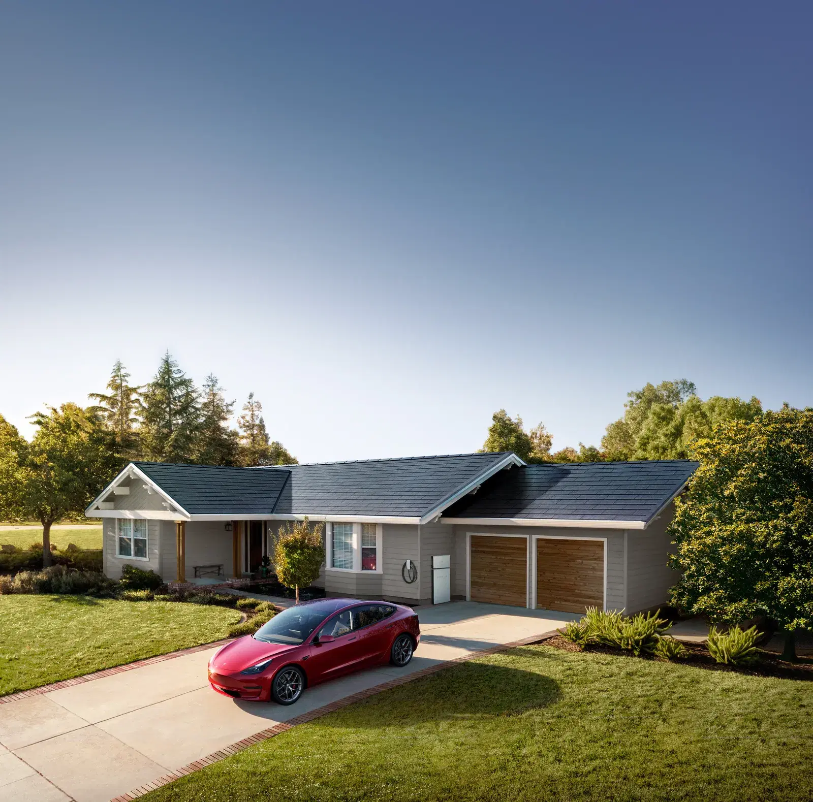 Ranch-style home with a dark glass solar-tile roof, a wall-mounted Powerwall by the garage and a red Tesla in the driveway.