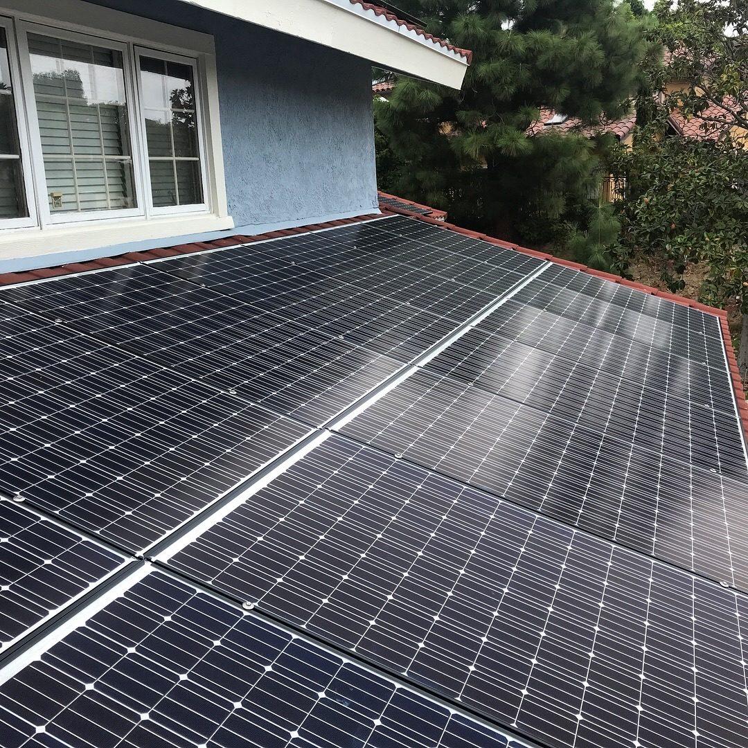 Solar panels installed close to the roofline of a blue stucco Southern California home