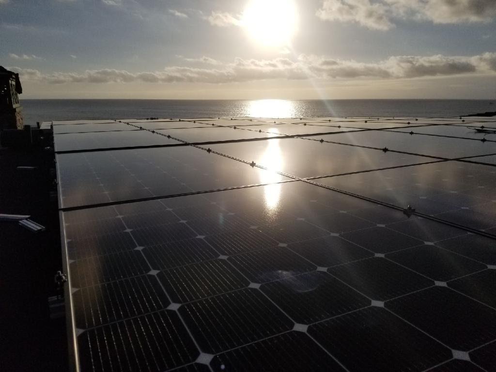 An OC Solar rooftop array overlooking the Pacific Ocean, bright sun reflecting off the panels