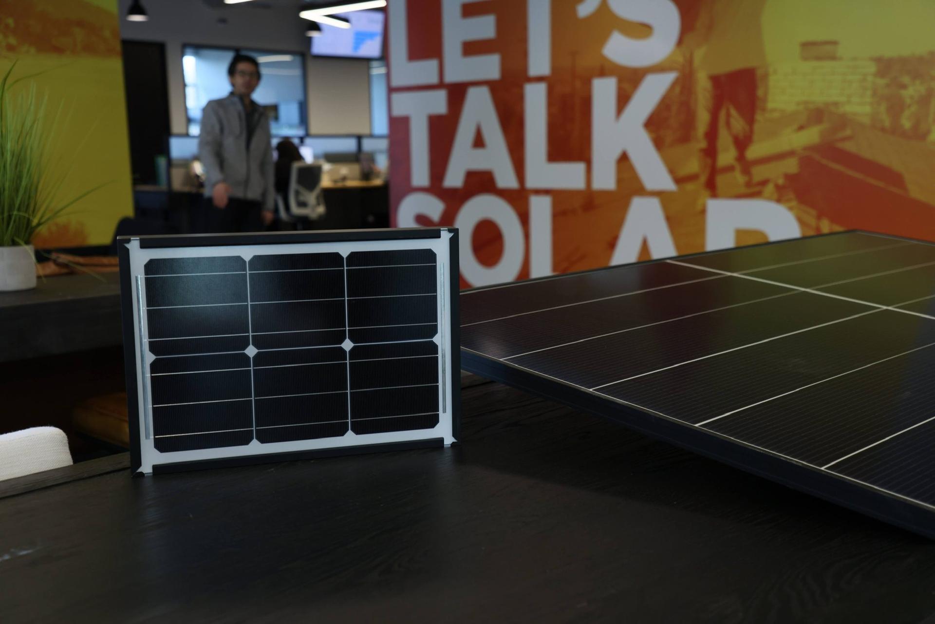 A small solar cell sample next to a full-size all-black panel in the OC Solar showroom